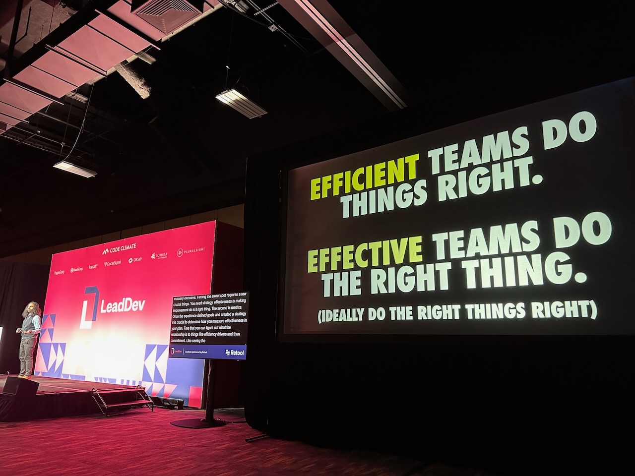 A stage setup for a conference talk with a large screen displaying the phrase 'Efficient teams do things right. Effective teams do the right thing'