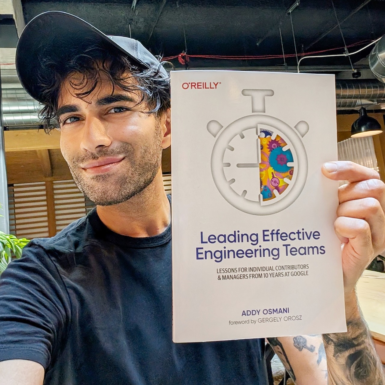 A person holding a book titled 'Leading Effective Engineering Teams' by Addy Osmani, smiling at the camera.